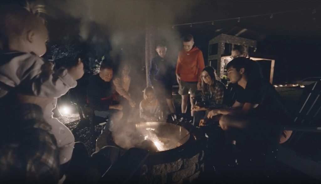 a large family sitting around a campfire at night outside of a cabinl