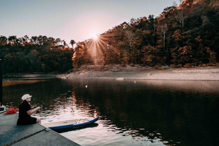 woman sits on the edge of a wooden pier on Lake Cumberland fishing, with a kayak nearby.