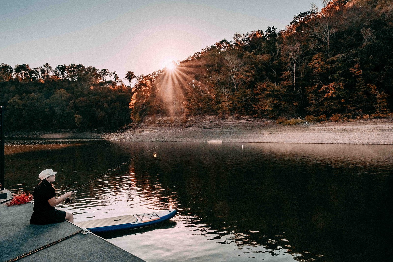 woman sits on the edge of a wooden pier on Lake Cumberland fishing, with a kayak nearby.