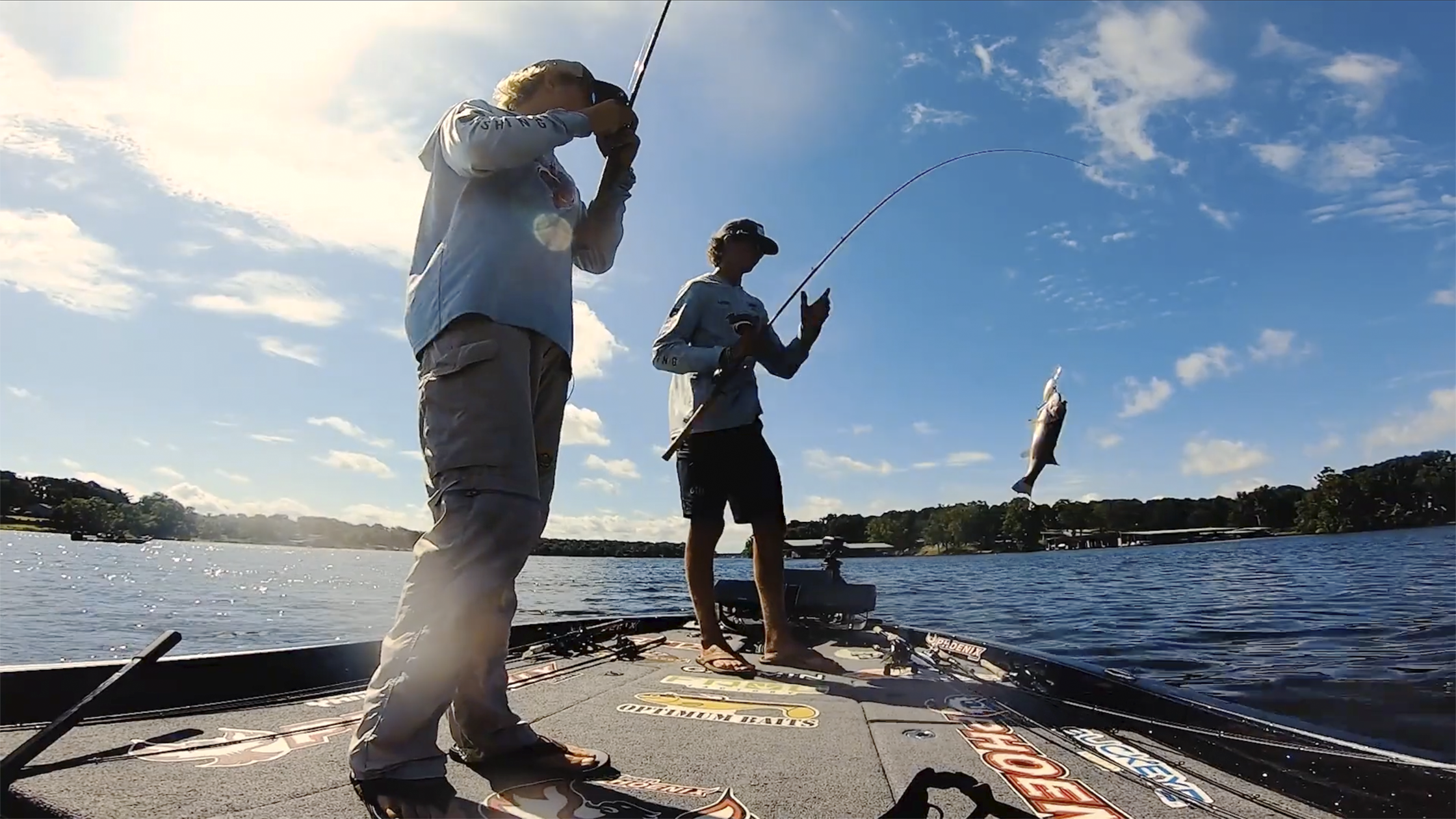 Two male high school anglers standing on a boat on the lake catching a fish